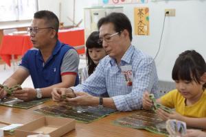 農糧署南區分署的分署長姚志旺(左)、客家委員會副主委鍾孔炤(右)與小朋友同樂體驗社區桌遊《農民好辛苦》